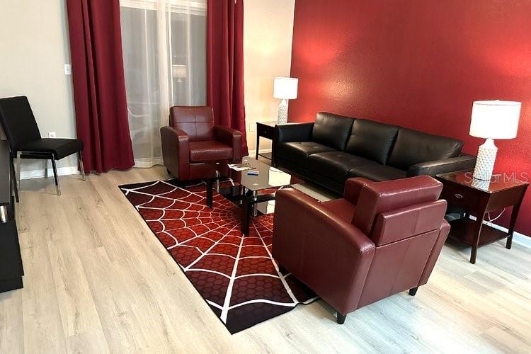 A living room features a red accent wall, a spiderweb-patterned rug, and leather furniture — 8125 RESORT VILLAGE DRIVE UNIT 51201, ORLANDO, FL