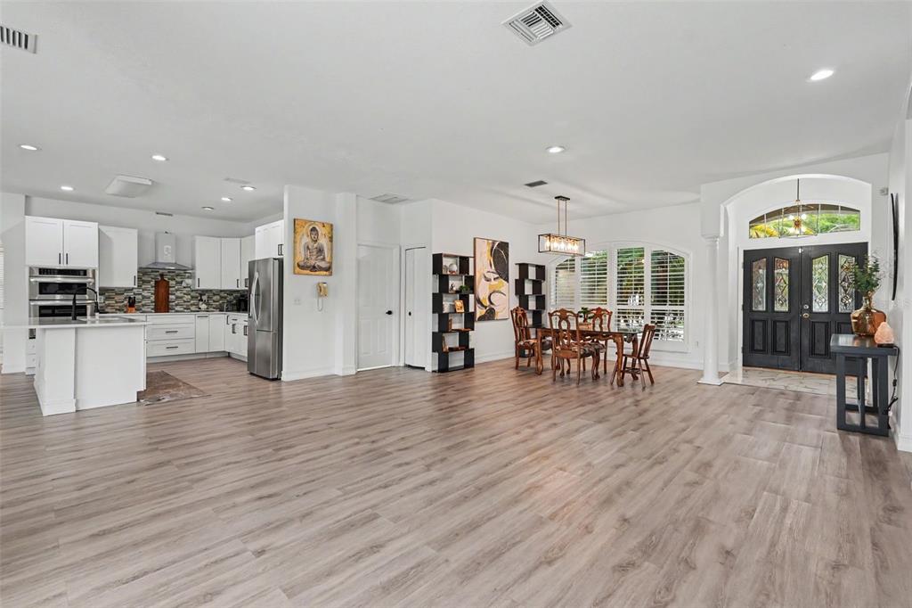 An open-concept kitchen and dining area with white cabinetry, wood-look flooring, and a dark front door — 12507 ROYAL DUBLIN AVENUE, ODESSA, FL