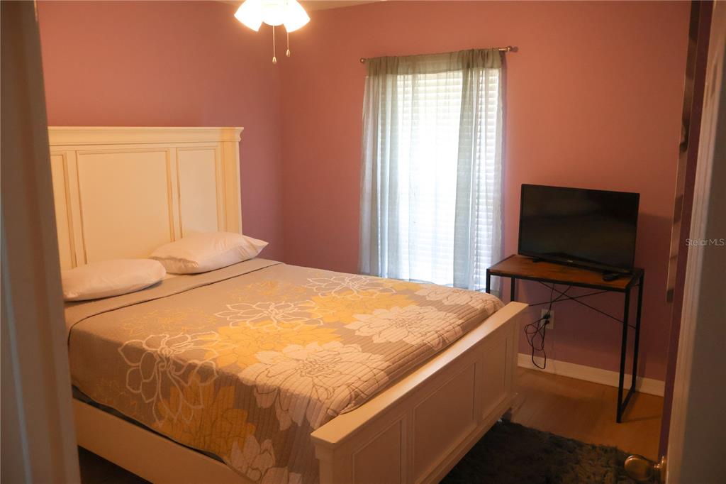 A bedroom features a white bed frame, floral bedding, pink walls, and a television stand — 5396 CARAMELLA DRIVE, ORLANDO, FL