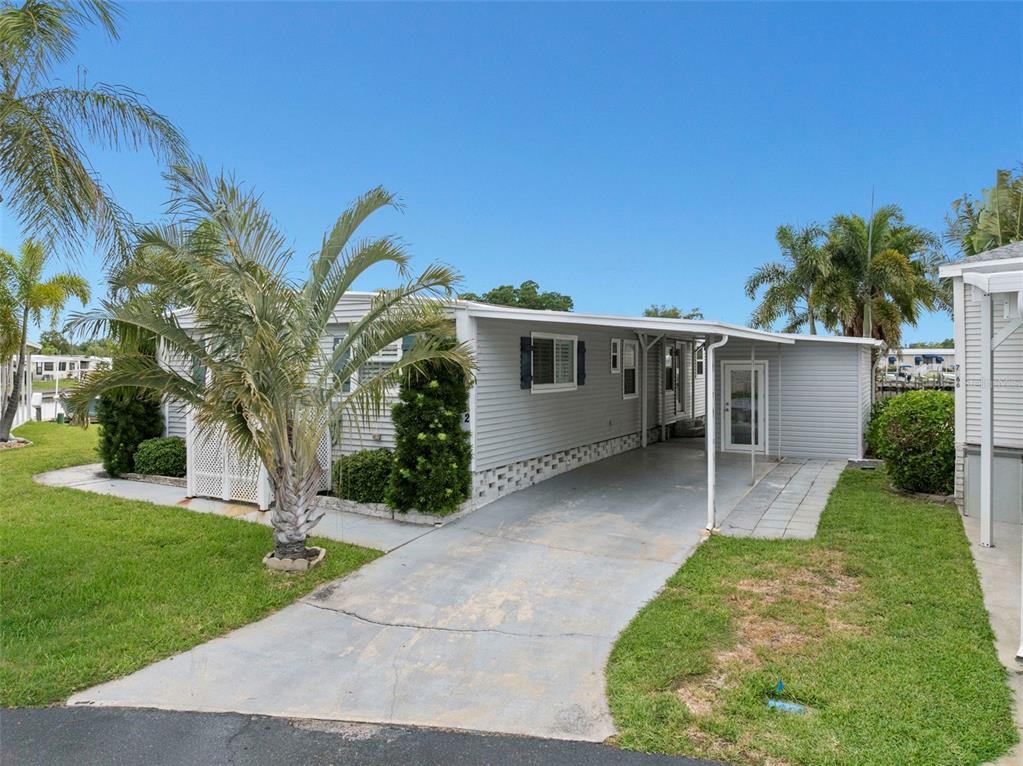 A light gray mobile home features a concrete driveway, a carport, and surrounding palm trees — 7162 MOUNT ARLINGTON DRIVE NE UNIT 417, ST PETERSBURG, FL