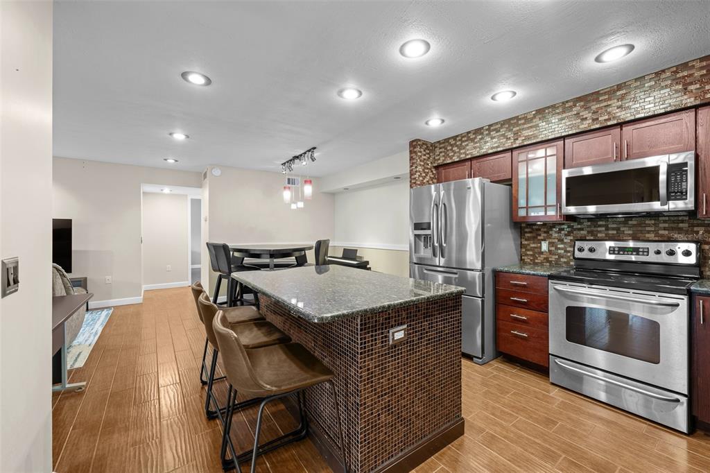 A kitchen features a granite-topped island with bar seating, stainless steel appliances, and tile flooring — 9481 HIGHLAND OAK DRIVE UNIT 1709, TAMPA, FL
