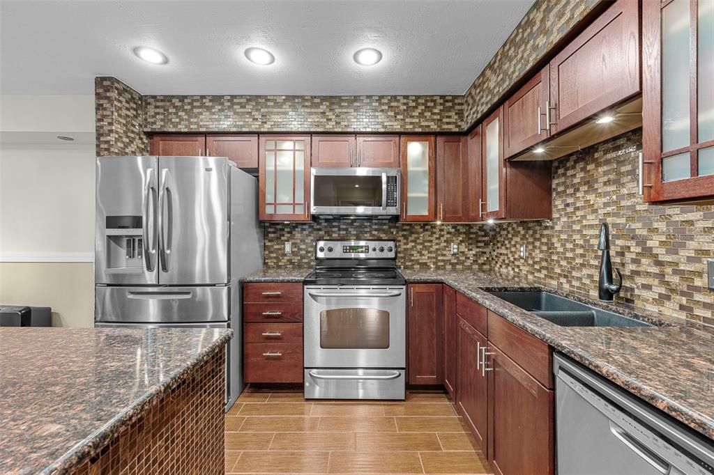 A kitchen features dark wood cabinets, granite countertops, stainless steel appliances, and a tiled backsplash — 9481 HIGHLAND OAK DRIVE UNIT 1709, TAMPA, FL