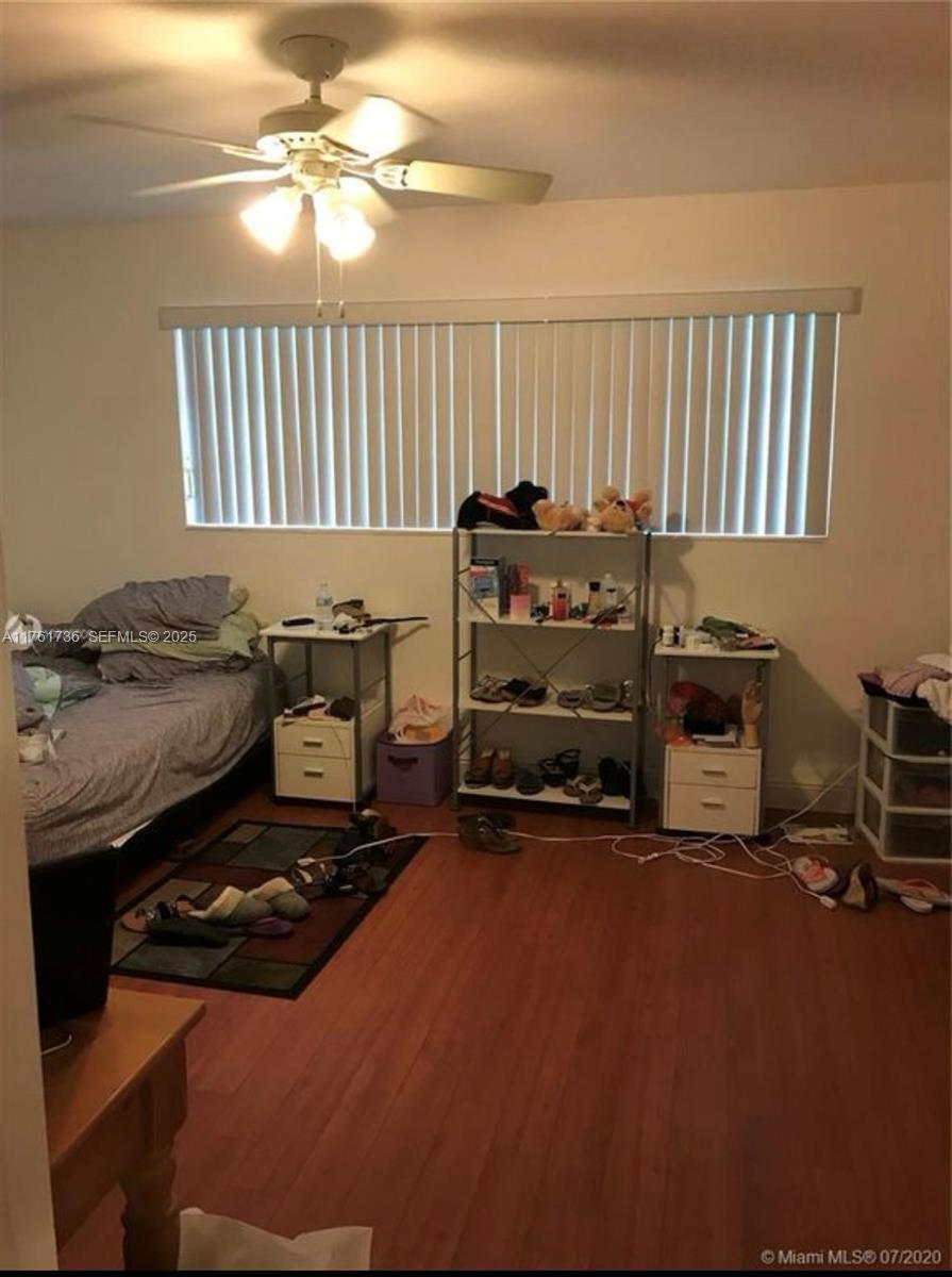 A bedroom features wood-look flooring, a ceiling fan, vertical blinds, and various storage furniture — 7344 SW 82nd St # C113, Miami FL 33143, MIAMI, FL