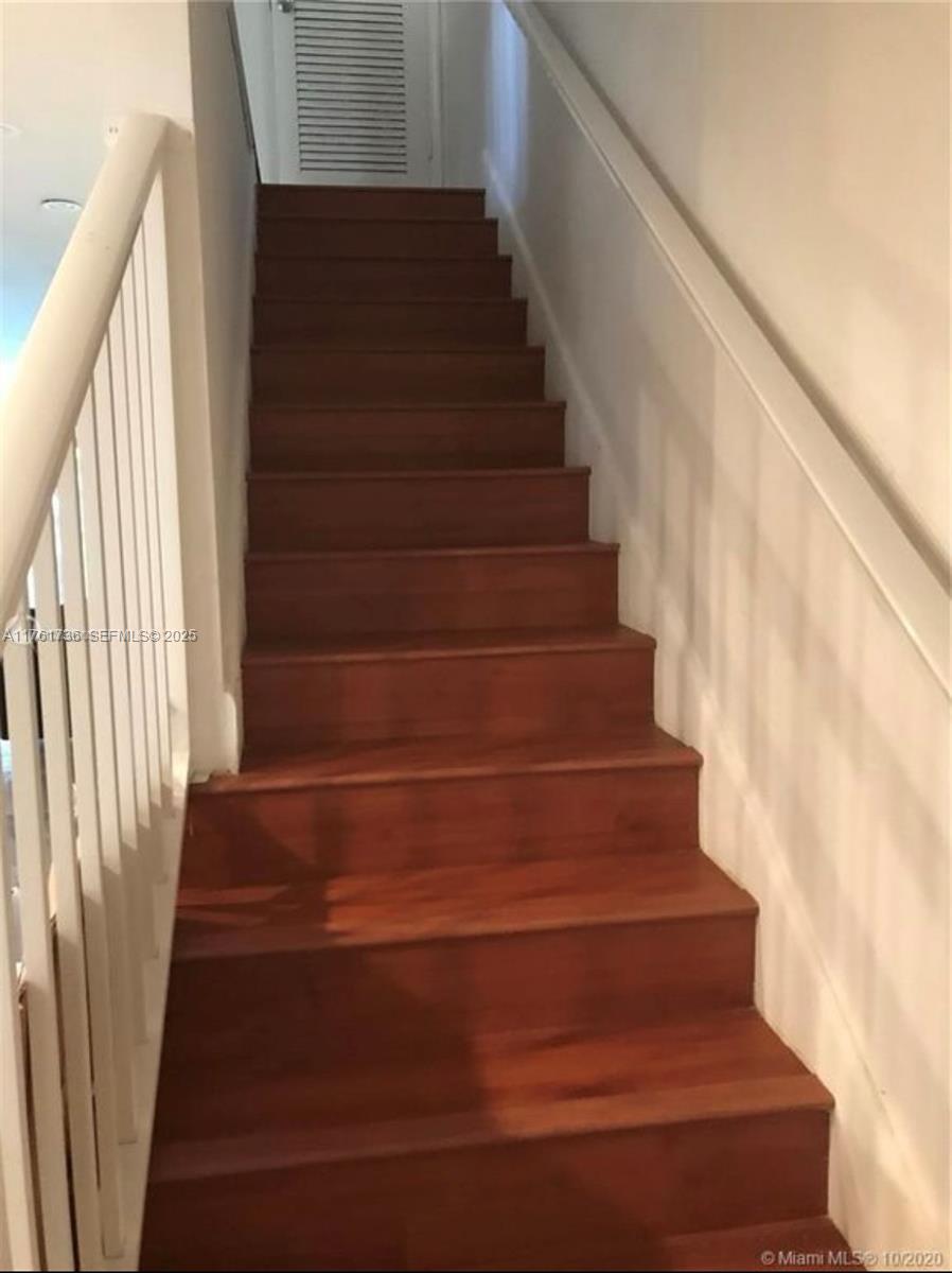 A straight wooden staircase with white railings leads to a landing with a louvered door — 7344 SW 82nd St # C113, Miami FL 33143, MIAMI, FL