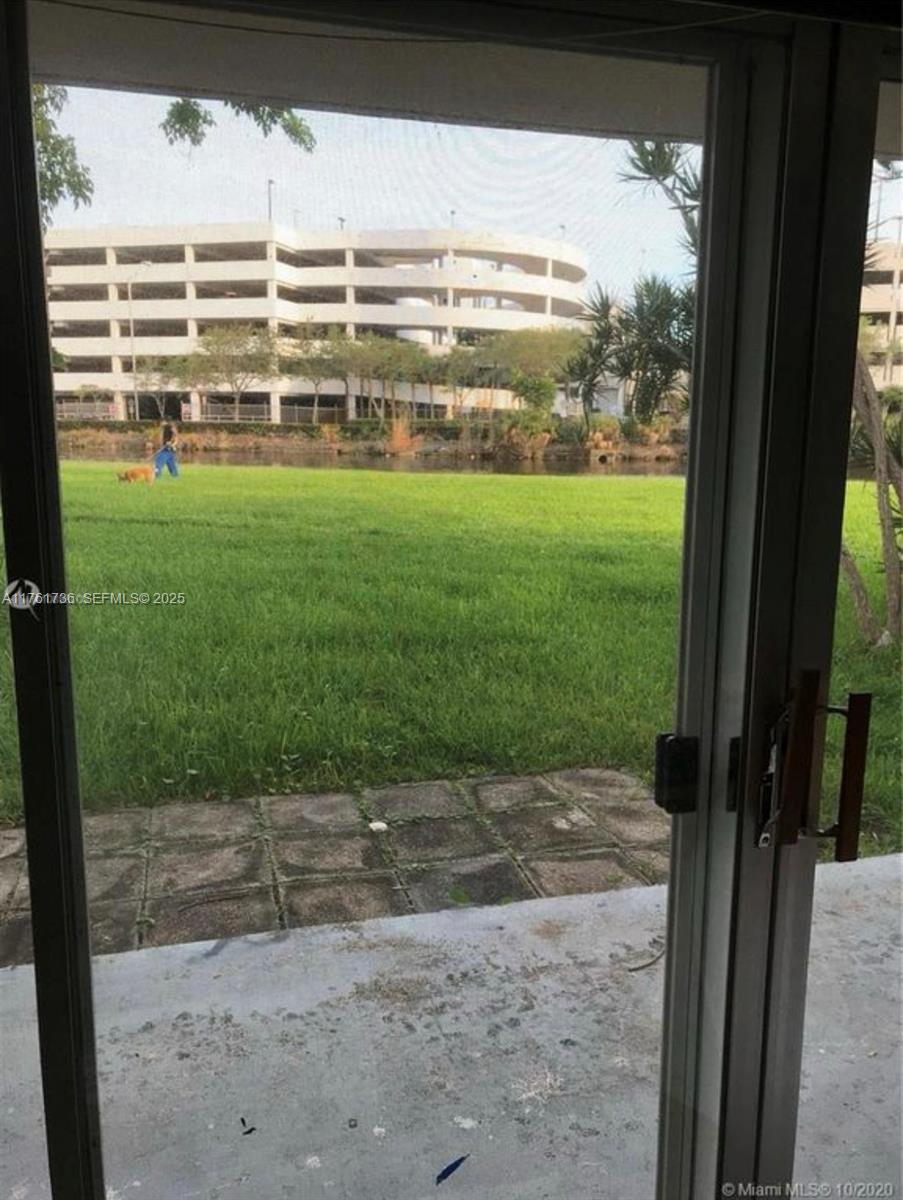 A view through a sliding glass door shows a grassy lawn, a pond, and a parking garage — 7344 SW 82nd St # C113, Miami FL 33143, MIAMI, FL