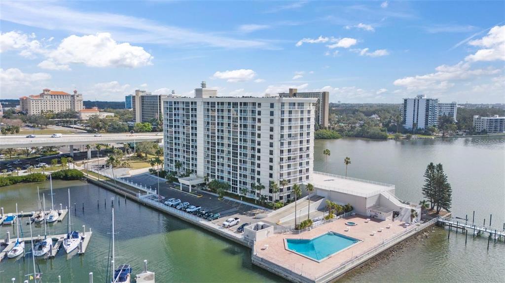 An aerial view shows a tall apartment building with a pool, parking lot, and marina — 100 PIERCE STREET UNIT 808, CLEARWATER, FL