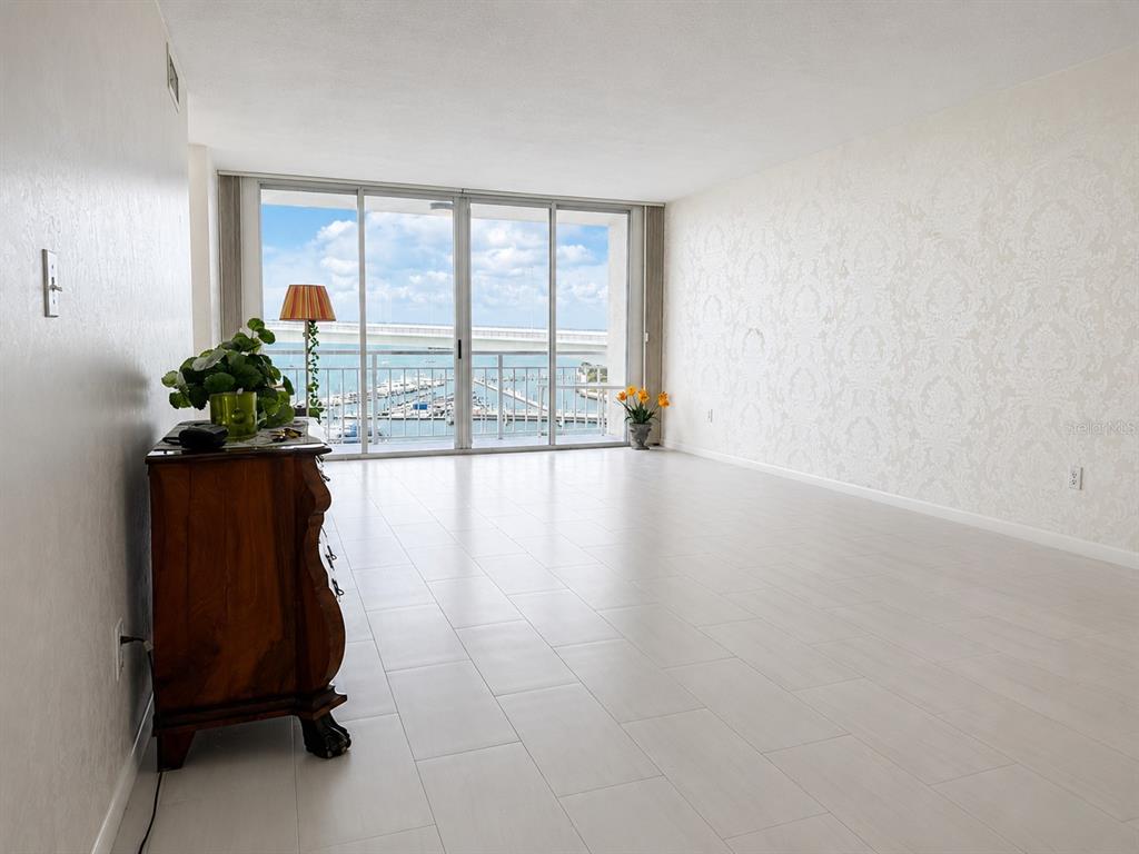 A bright living room features light tile flooring, patterned wallpaper, and a balcony overlooking water — 100 PIERCE STREET UNIT 808, CLEARWATER, FL