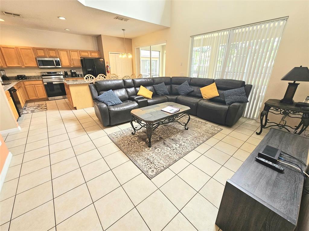 An open-concept living room and kitchen with tile flooring, a sectional sofa, and wood cabinetry — 207 HIDEAWAY BEACH LANE, KISSIMMEE, FL