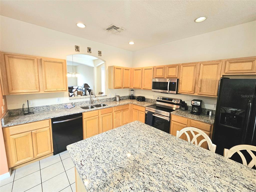 A kitchen features light wood cabinets, granite countertops, a kitchen island, and black appliances — 207 HIDEAWAY BEACH LANE, KISSIMMEE, FL