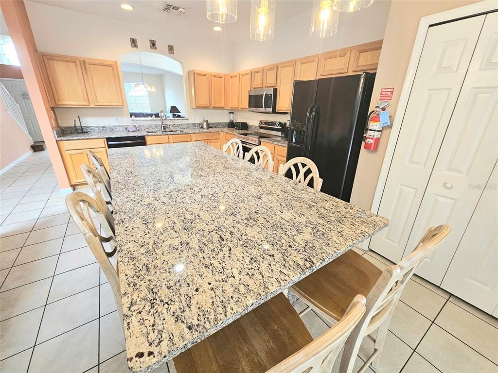 A kitchen features a large granite-topped island, light wood cabinetry, and black appliances — 207 HIDEAWAY BEACH LANE, KISSIMMEE, FL