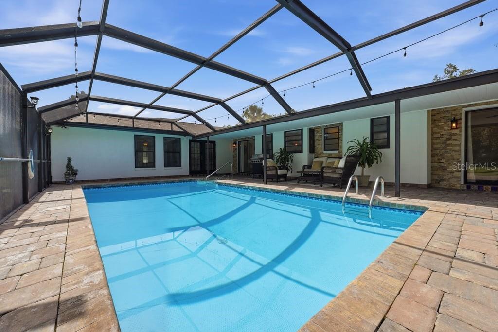 A rectangular swimming pool sits inside a screened-in patio with stone pavers and outdoor furniture — 15562 MAYNARD AVENUE, PORT CHARLOTTE, FL