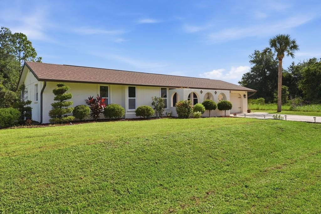 A single-story white house with a brown roof sits on a large, grassy lawn — 15562 MAYNARD AVENUE, PORT CHARLOTTE, FL