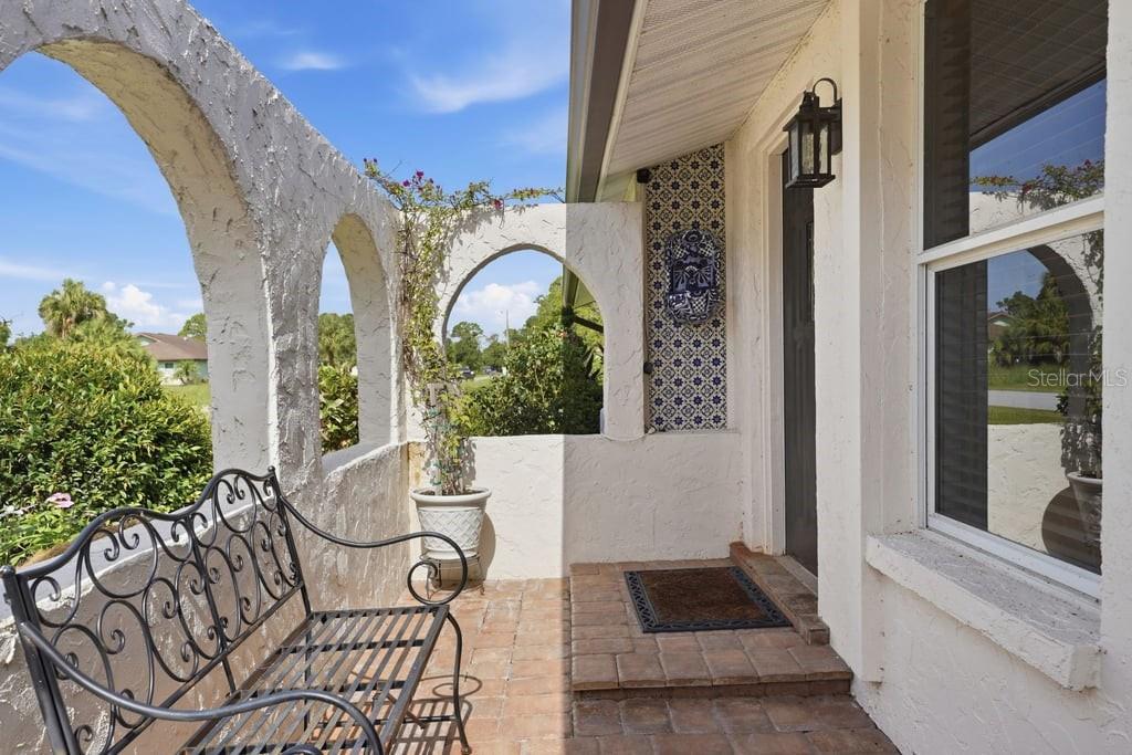 A covered porch features arched stucco walls, a brick floor, and a decorative tiled accent wall — 15562 MAYNARD AVENUE, PORT CHARLOTTE, FL