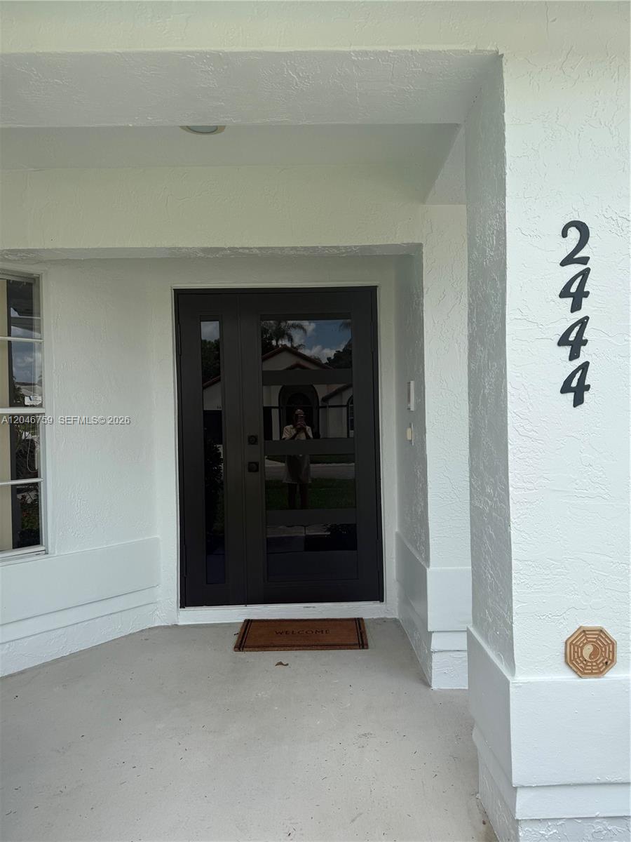 A modern dark front door with horizontal glass panels sits under a covered entryway — 2444 Stonegate Dr, Wellington FL 33414, WELLINGTON, FL
