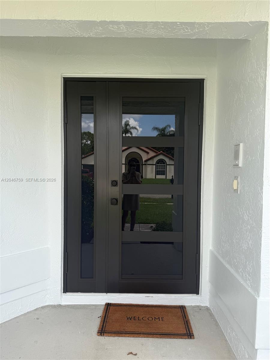 A modern dark-framed front door with glass panels sits on a concrete porch — 2444 Stonegate Dr, Wellington FL 33414, WELLINGTON, FL