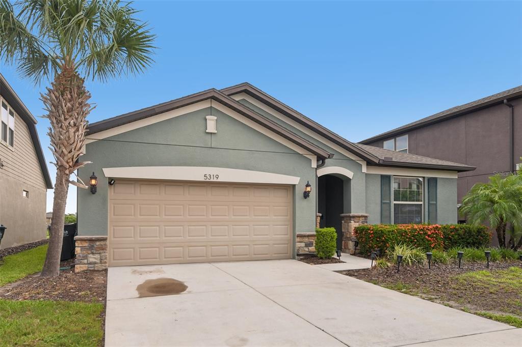 A single-story house with a sage green exterior, a two-car garage, and a palm tree — 5319 FALLEN LEAF DRIVE, RIVERVIEW, FL