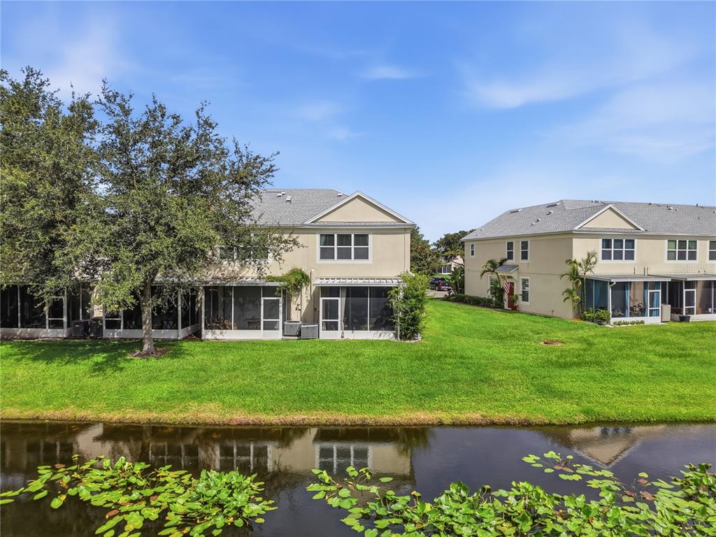 Two-story townhouses with screened-in lanais sit behind a pond with lily pads — 2528 GLENRISE PLACE, WESLEY CHAPEL, FL
