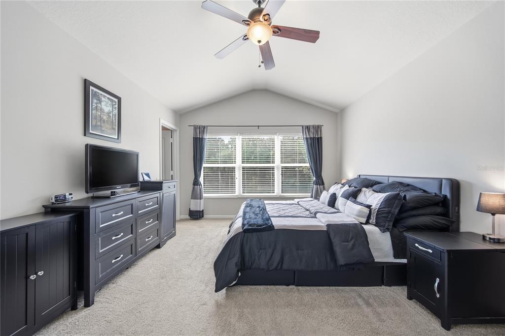 A bedroom with a vaulted ceiling, black furniture, a large bed, and a window with curtains — 2528 GLENRISE PLACE, WESLEY CHAPEL, FL