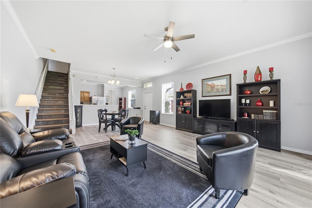 A living room with dark leather furniture, a black area rug, and stairs leading upward — 2528 GLENRISE PLACE, WESLEY CHAPEL, FL