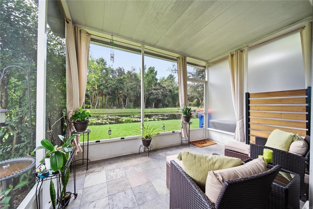 A screened-in porch with tiled flooring overlooks a pond and wooded area — 2528 GLENRISE PLACE, WESLEY CHAPEL, FL