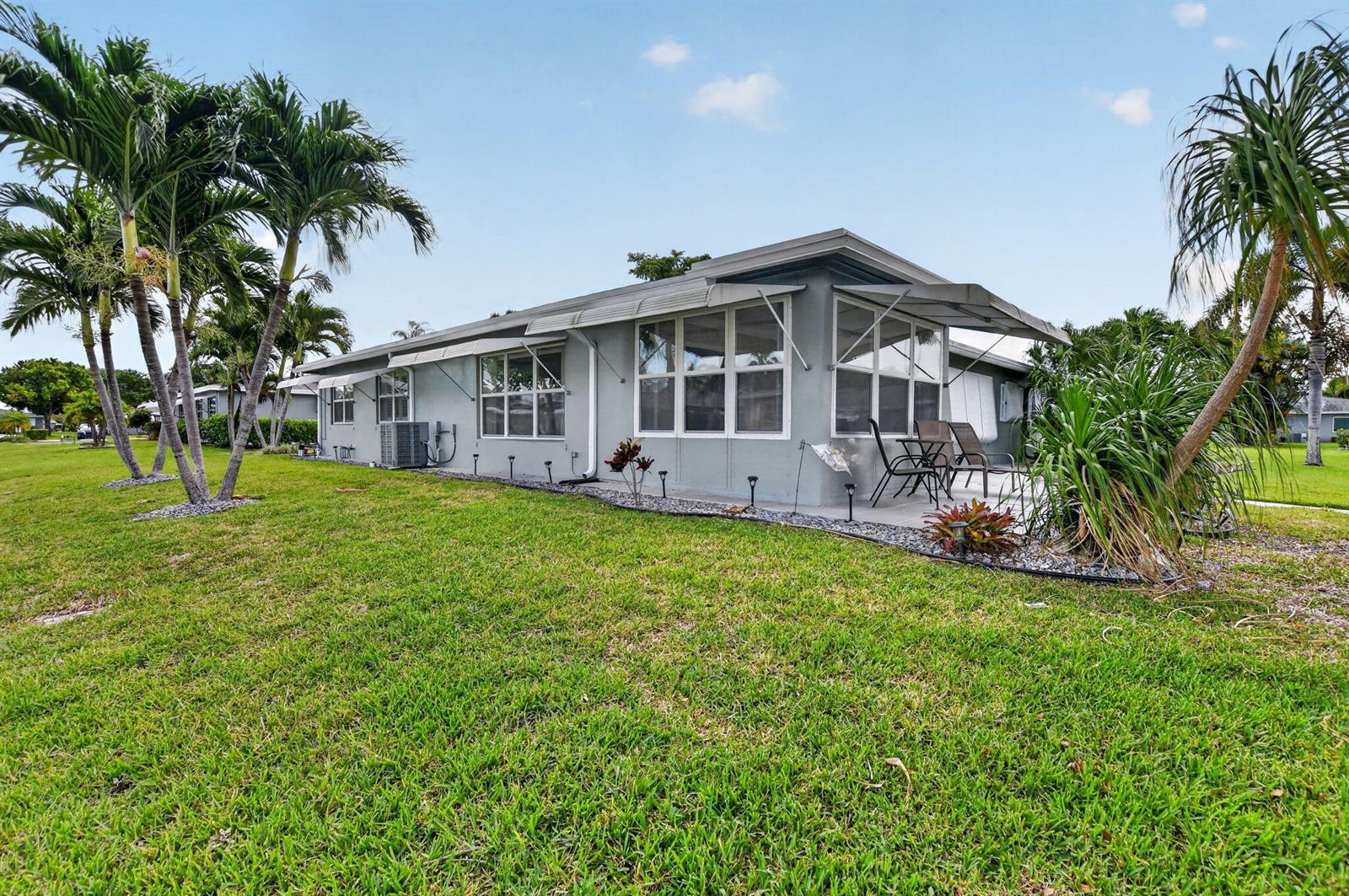 A single-story gray house with a patio and palm trees sits on a grassy lawn — 920 South Drive # A, Delray Beach FL 33445, DELRAY BEACH, FL