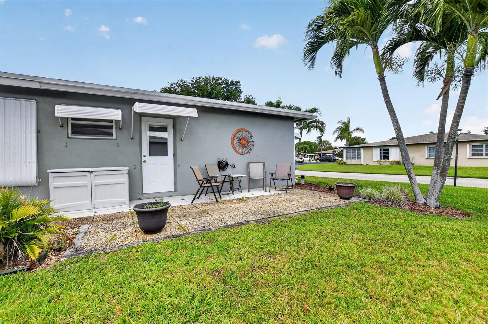 A gray exterior wall features a white door, a small patio, and two palm trees — 920 South Drive # A, Delray Beach FL 33445, DELRAY BEACH, FL