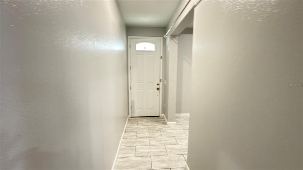 A hallway with light gray walls and light-colored rectangular floor tiles leads to a door — 2704 W SAINT CONRAD STREET, TAMPA, FL