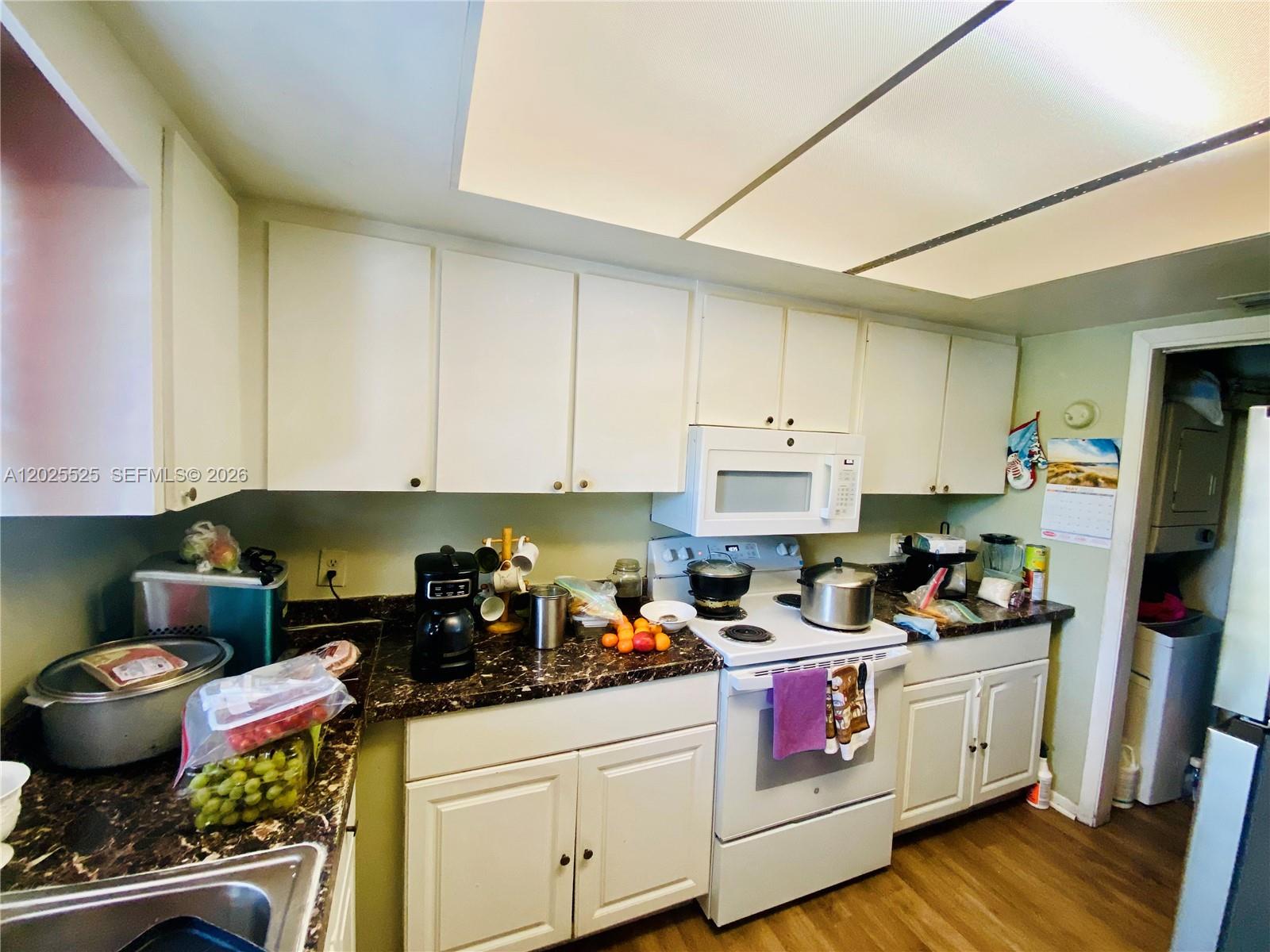 A kitchen features white cabinets, dark marble-patterned countertops, and white appliances — 1702 S Dixie Hwy # 15, Lake Worth FL 33460, LAKE WORTH, FL