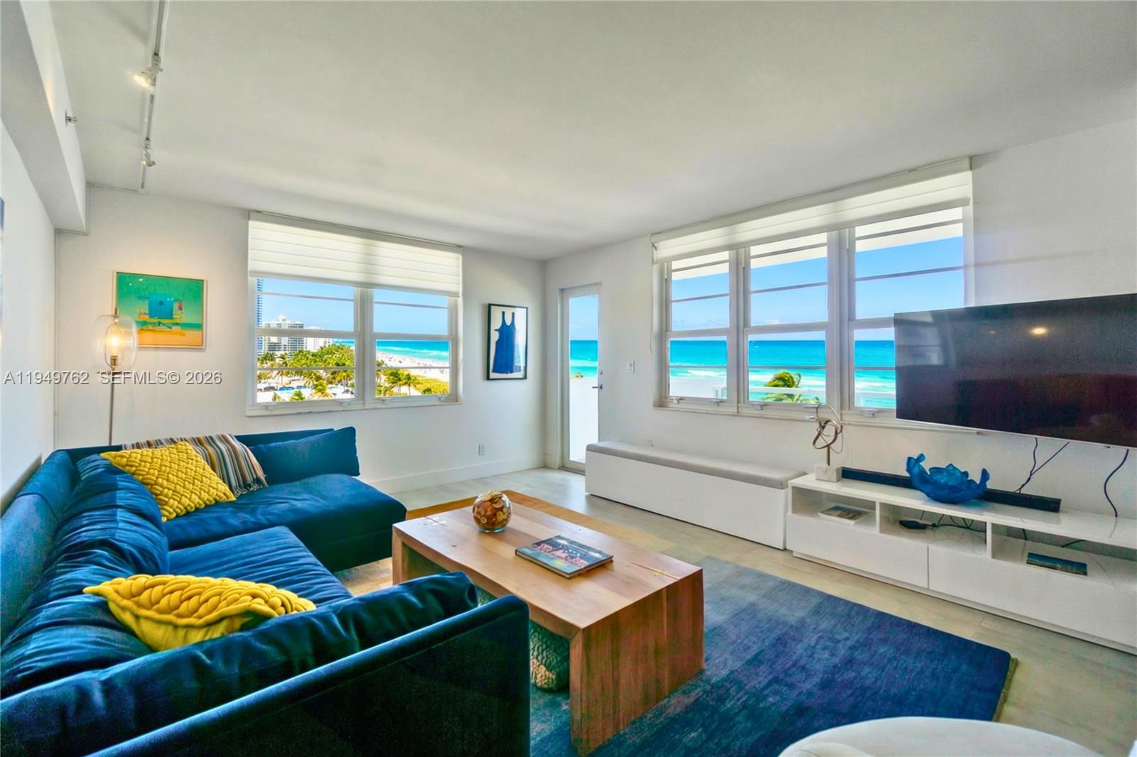 A living room features a blue sectional sofa, wooden coffee table, and ocean views — 100 Lincoln Rd # 1447, Miami Beach FL 33139, MIAMI BEACH, FL