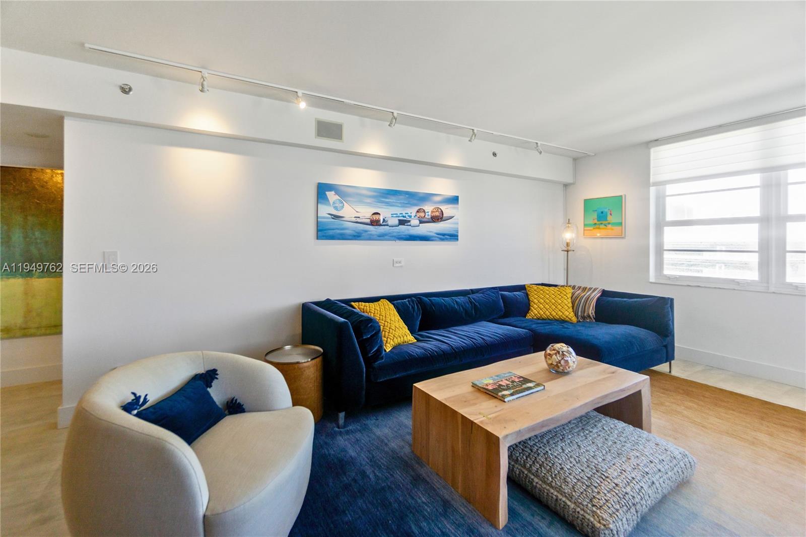A living room features a blue sectional sofa, a light-colored armchair, and a wooden coffee table — 100 Lincoln Rd # 1447, Miami Beach FL 33139, MIAMI BEACH, FL