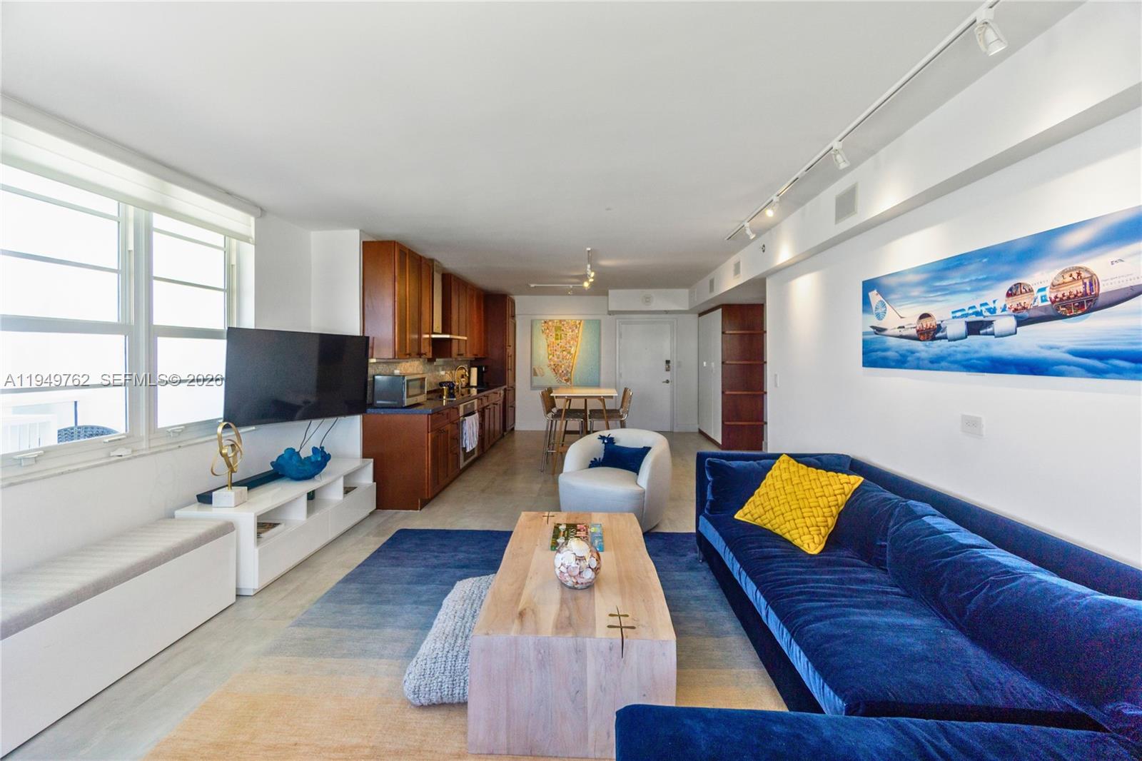 An open-concept living room and kitchen feature a blue sofa, wood coffee table, and cabinetry — 100 Lincoln Rd # 1447, Miami Beach FL 33139, MIAMI BEACH, FL