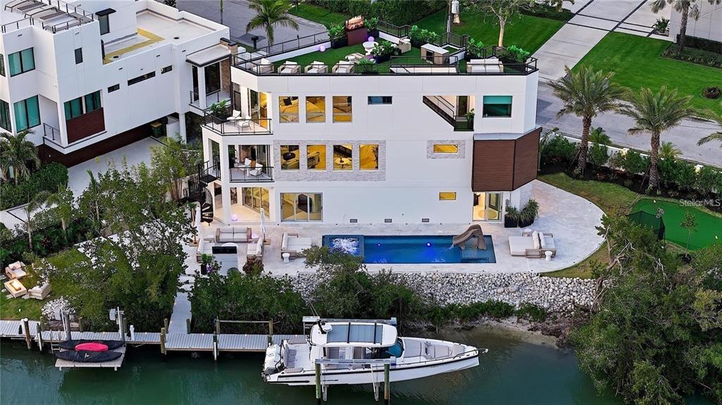 An aerial view shows a modern three-story house with a rooftop deck, pool, and boat dock — 1406 TANGIER WAY, SARASOTA, FL