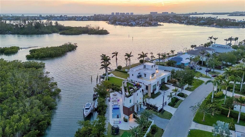 An aerial view shows a modern multi-story waterfront home with a pool and private dock — 1406 TANGIER WAY, SARASOTA, FL