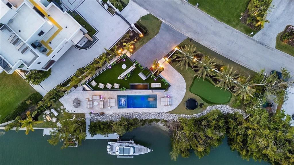 An aerial view shows a waterfront backyard with a pool, putting green, and boat dock — 1406 TANGIER WAY, SARASOTA, FL