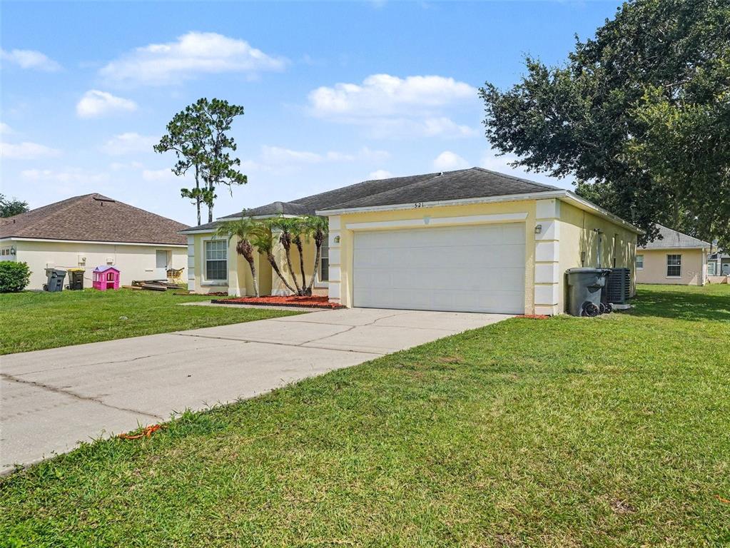 A yellow single-story house with a two-car garage and a concrete driveway — 521 EAGLE COURT, KISSIMMEE, FL
