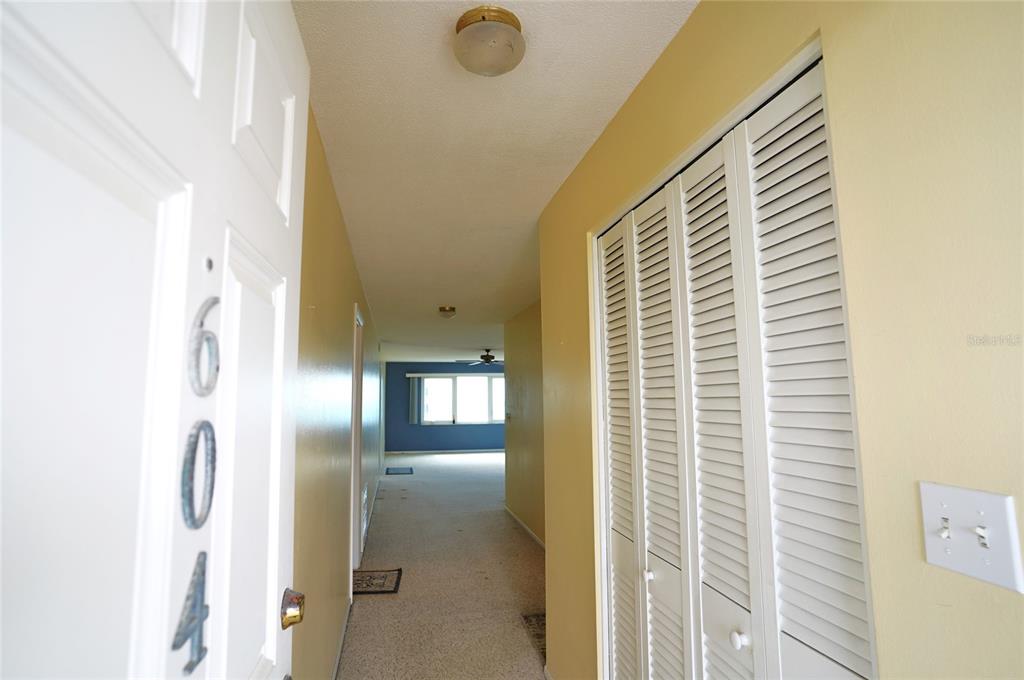 A hallway with a white door, louvered closet doors, and a view into a living area — 500 THE ESPLANADE N UNIT 604, VENICE, FL