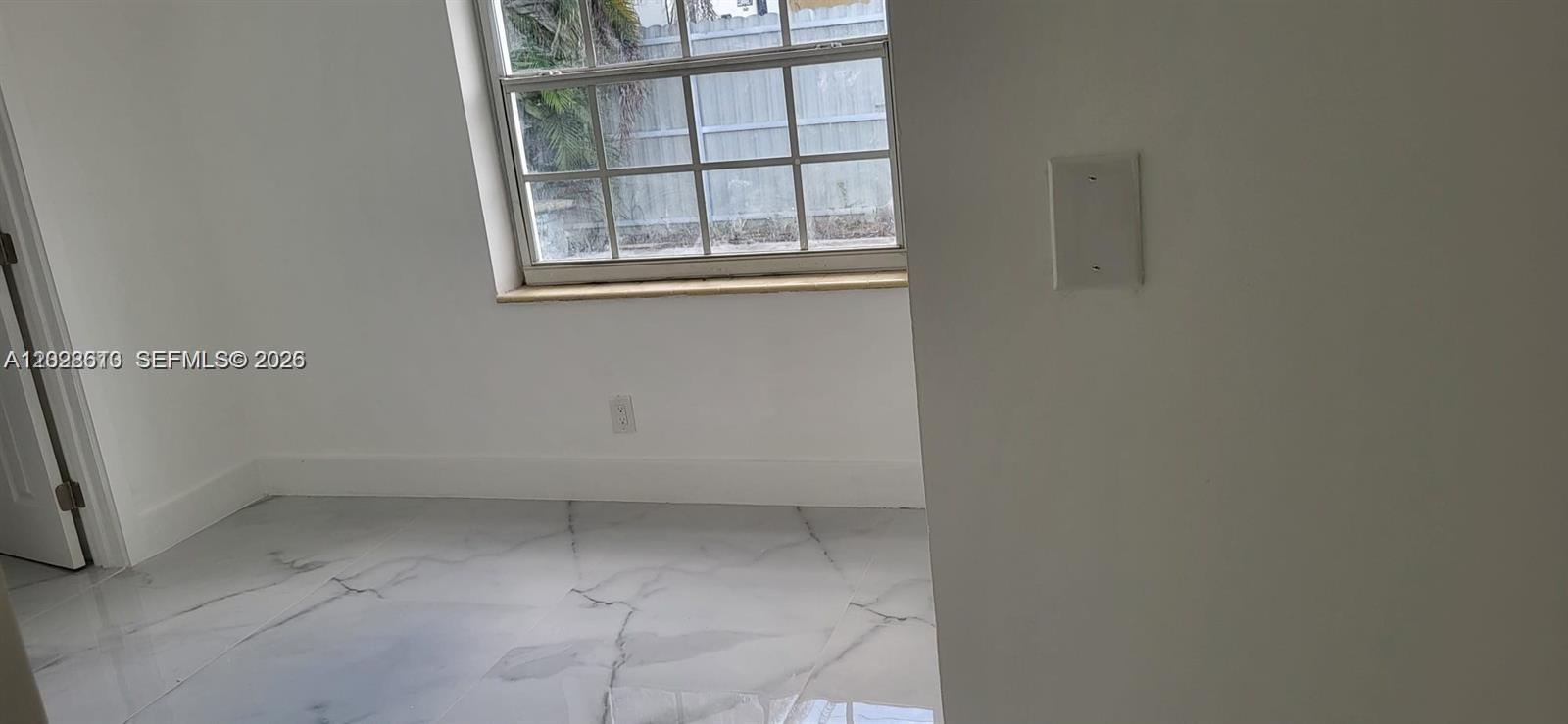 A room with white walls, marble-patterned tile flooring, and a window overlooking a fence — 712 Hialeah Dr, Hialeah FL 33010, HIALEAH, FL