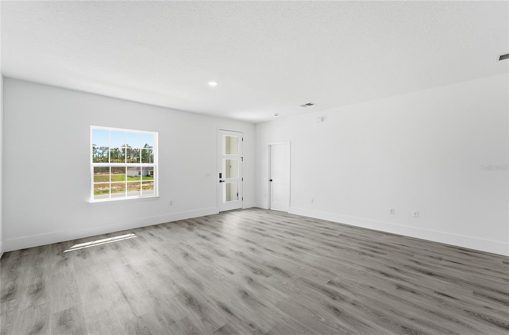 A bright, empty living room features white walls, gray wood-look flooring, and a glass-paneled door — 2861 W DELLWOOD STREET, CITRUS SPRINGS, FL