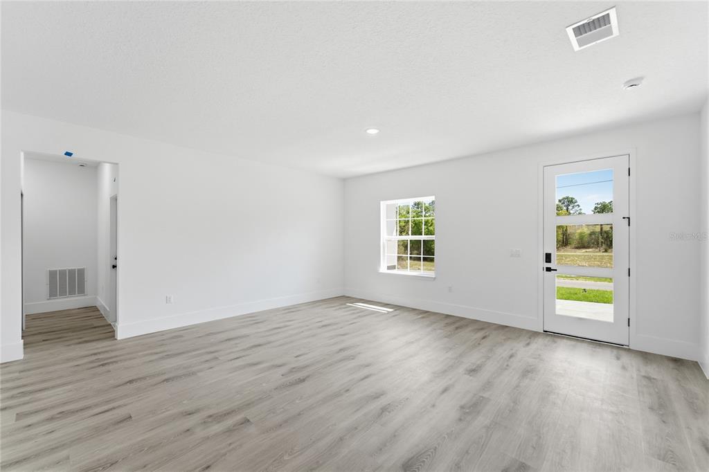 An empty room features white walls, light wood-look flooring, a window, and a glass-paneled door — 2861 W DELLWOOD STREET, CITRUS SPRINGS, FL