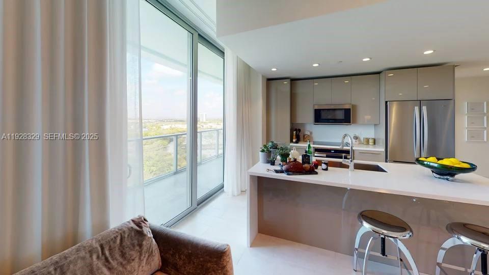 A modern kitchen with glossy cabinets and a breakfast bar overlooks a balcony with views — 2000 Metropica Way # 1701, Sunrise FL 33323, SUNRISE, FL