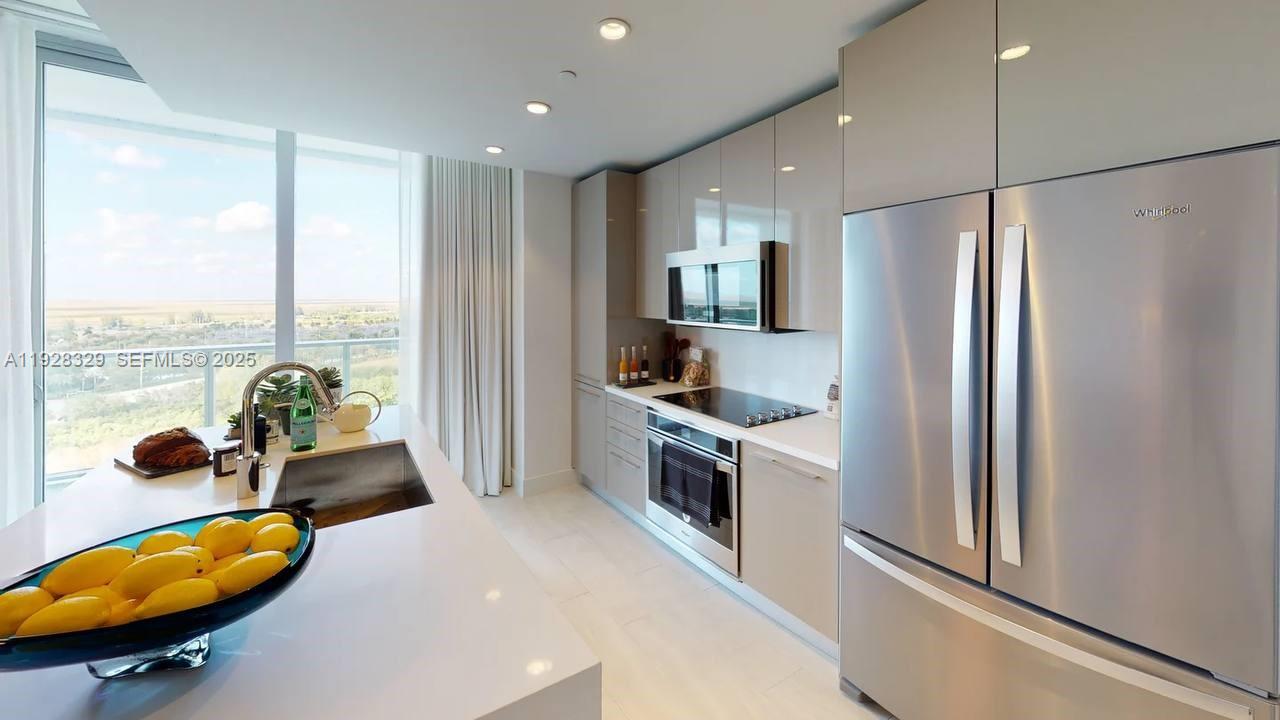 A modern kitchen features light cabinetry, stainless steel appliances, and a large island with lemons — 2000 Metropica Way # 1701, Sunrise FL 33323, SUNRISE, FL