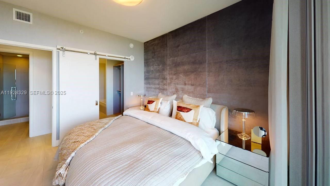 A bedroom features a bed with white bedding, a dark accent wall, and sliding doors — 2000 Metropica Way # 1701, Sunrise FL 33323, SUNRISE, FL