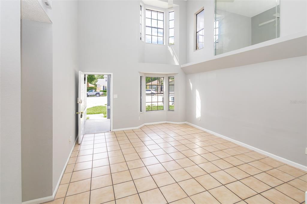 A bright, high-ceilinged living room features light tile flooring, a bay window, and an entryway — 4226 CLOVERLEAF PLACE, CASSELBERRY, FL