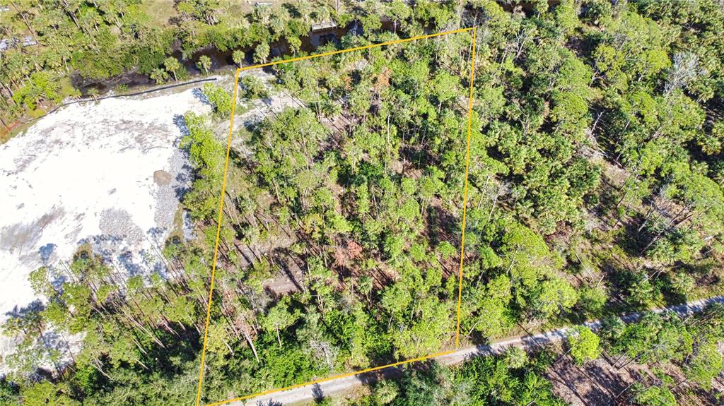 An aerial view shows a wooded, rectangular plot of land outlined in yellow — 9051 CALOOSA DRIVE, VENICE, FL