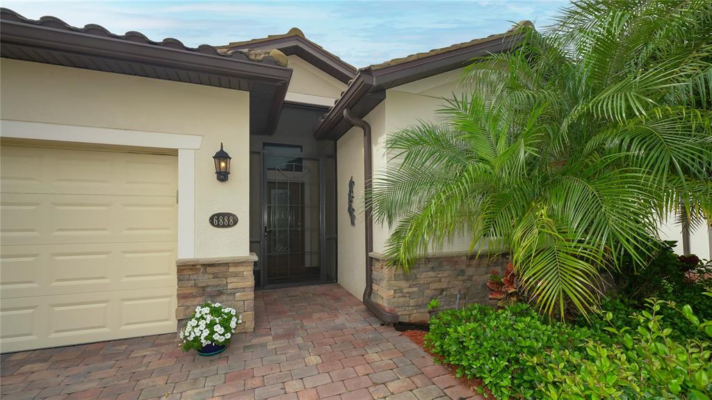 The exterior of a house features a garage, a stone-accented entryway, and a palm tree — 6888 WILLOWSHIRE WAY, BRADENTON, FL