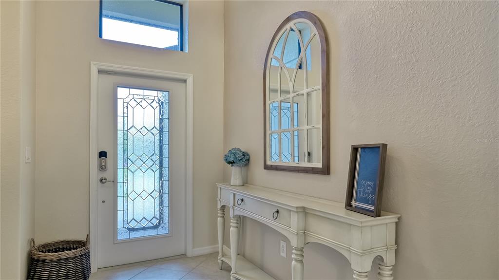 An entryway features a white front door, a console table, and an arched wall mirror — 6888 WILLOWSHIRE WAY, BRADENTON, FL