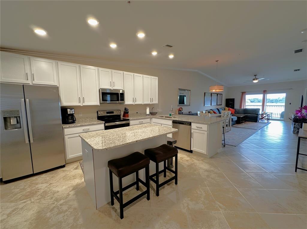 A kitchen with white cabinets, granite countertops, and a center island opens to a living area — 14050 HERITAGE LANDING BOULEVARD UNIT 226, PUNTA GORDA, FL