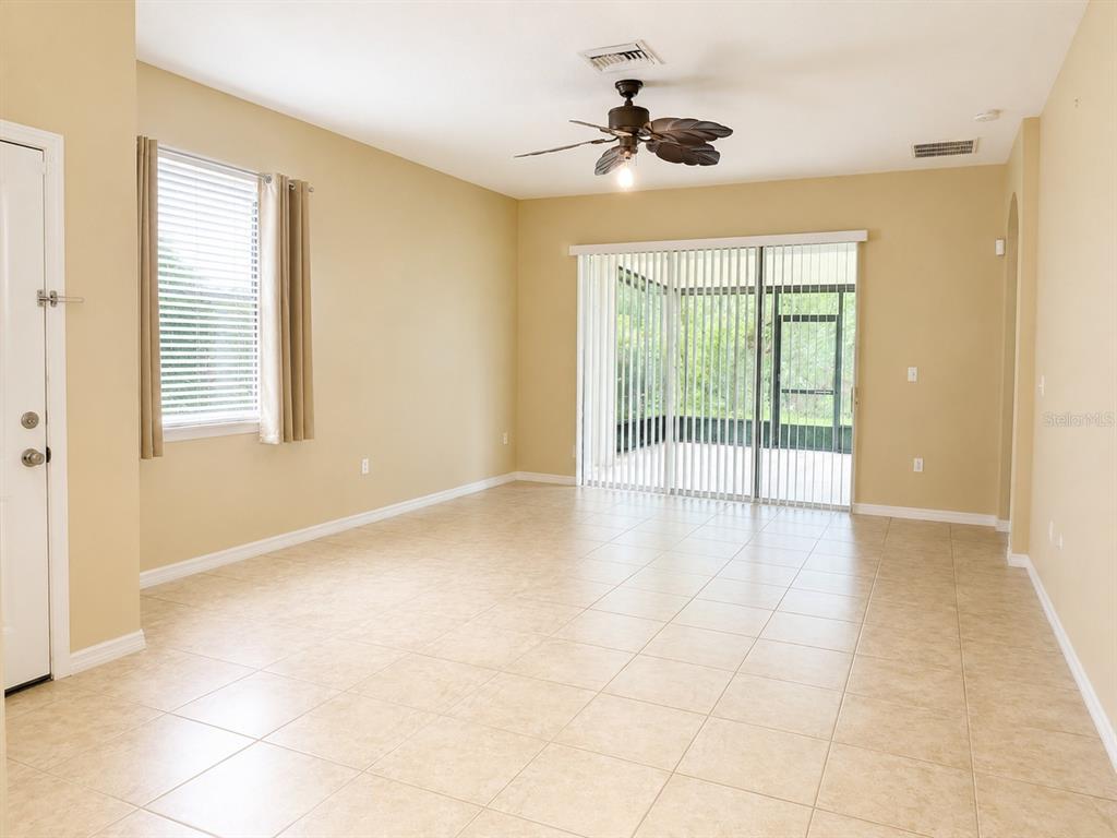 An empty living room features beige tile flooring, a ceiling fan, and sliding glass doors — 7436 SURREY PINES DRIVE, APOLLO BEACH, FL