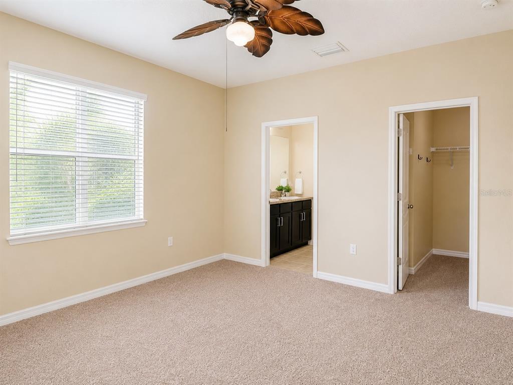 A bedroom with beige carpet, a ceiling fan, a window with blinds, and two doorways — 7436 SURREY PINES DRIVE, APOLLO BEACH, FL