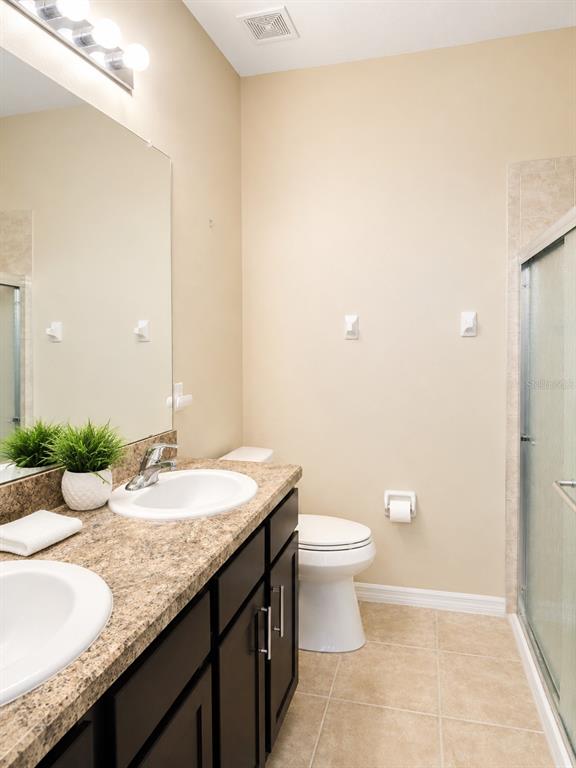 A bathroom features a double vanity with dark cabinets, a granite countertop, and a shower stall — 7436 SURREY PINES DRIVE, APOLLO BEACH, FL